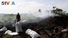 Deo Ssenyimba stands near a heap of burning charcoal in Gulu, Uganda, May 27, 2023. (AP Photo/Hajarah Nalwadda)