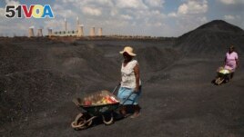 FILE - Women push wheelbarrows atop a coal mine dump at the coal-powered Duvha power station, near Emalahleni east of Johannesburg, Nov. 17, 2022. (AP Photo/Denis Farrell, File)