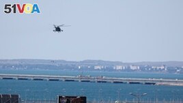 A Russian military helicopter flies over damaged parts of an automobile link of the Crimean Bridge connecting the Russian mainland and the Crimean peninsula over the Kerch Strait on July 17, 2023. (AP Photo)
