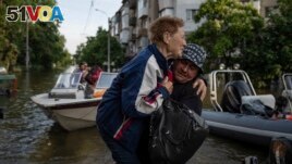 FILE - A volunteer carries a woman as she is evacuated from a flooded Kardashynka village of the bank Dnipro river, in Kherson, Ukraine on June 9, 2023. (AP Photo/Evgeniy Maloletka)