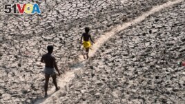 FILE - A man and a boy walk across a dried-up bed of river Yamuna in New Delhi, India, May 2, 2022. (AP Photo/Manish Swarup, File)