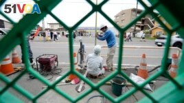 Workers set up a barricade near the Lawson convenience store, background, Tuesday, April 30, 2024, at Fujikawaguchiko town, central Japan. (AP Photo/Eugene Hoshiko)