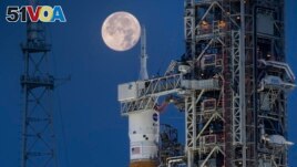 A full moon is seen behind the Artemis I Space Launch System (SLS) and Orion spacecraft, atop the mobile launcher, at NASA's Kennedy Space Center in Florida on June 14, 2022. (Cory Huston/NASA via AP)