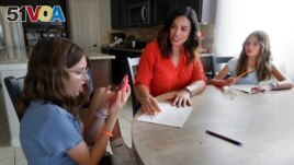 Giada Gambino, 10, left, uses her smartphone to consult a voice assistant about a math problem. (AP Photo/Michael Wyke)