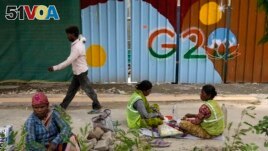Laborers take a lunch break near a construction site covered with G20 summit logo in New Delhi, India, Thursday, Aug. 24, 2023. (AP Photo/Manish Swarup)