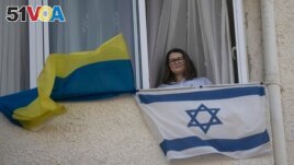 Tatyana Prima, who fled Mariupol, Ukraine, poses for a portrait with her national flag and the Israeli flag she displays outside of her apartment window in Ashkelon, southern Israel, Wednesday, Nov. 8, 2023. (AP Photo/Maya Alleruzzo)