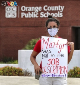 FILE - In this Tuesday, July 7, 2020 file photo, Rachel Bardes holds a sign in front of the Orange County Public Schools headquarters as teachers protest with a car parade in Orlando, Fla. (Joe Burbank/Orlando Sentinel via AP, File)