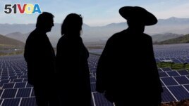 FILE - Locals walk past solar panels during the opening ceremony of the largest solar power plant of Chile's capital, in Santiago July 19, 2017. (REUTERS/Ivan Alvarado)