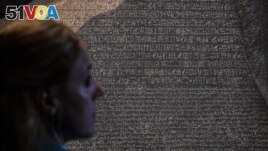 A member of the British Museum staff looks at the Rosetta Stone on Oct. 11, 2022, displayed for the exhibition Hieroglyphs: Unlocking Ancient Egypt, which runs at the London museum Oct. 13 through Feb. 19, 2023. (Photo by CARLOS JASSO / AFP)