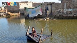 A girl sits on a cot as she crosses a flooded street at Sohbatpur in Jaffarabad district of Balochistan province on October 4, 2022. (Photo by Fida HUSSAIN / AFP)