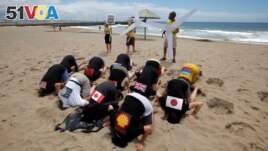 FILE - Environmental activists with flags on their backs bury their heads in the sand on Durban's beachfront, December 2, 2011. The protest aimed to highlight nations failing to act effectively to prevent climate change. (REUTERS/Mike Hutchings)