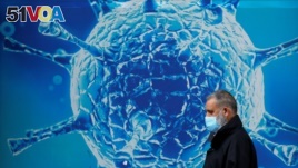 A man wearing a protective face mask walks past an illustration of a virus outside a regional science centre. (REUTERS/Phil Noble)