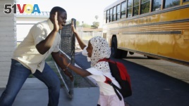 Samuel Lavi, left, a Congolese native who is a teaching assistant and family engagement liaison, greets first grader Kediga Ahmed as she arrives at the Valencia Newcomer School attend class, Oct. 17, 2019, in Phoenix. (AP Photo/Ross D. Franklin)