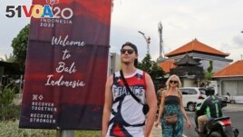 FILE - Tourists walk past a G20 banner in Nusa Dua, Bali, Indonesia on Friday, Nov. 11, 2022. The tropical island's ailing tourism industry returned after a two-year closure due to the pandemic. (AP Photo/Firdia Lisnawati)