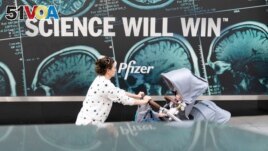 A woman pushes a baby in a stroller past a sign hanging outside Pfizer headquarters in New York, Monday, May 23, 2022. American health officials said Sunday that Pfizer's COVID-19 vaccine appears to be safe and effective for children under 5. (AP Photo/Mary Altaffer)