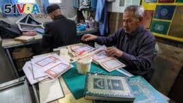 Libyan restorer of the Holy Koran Khaled al-Drebi (R), assembles pages together to be glued into a volume during a workshop on the restoration of copies of Islam's holy book, in Libya's capital Tripoli on March 22, 2022. (Photo by Mahmud Turkia / AFP)