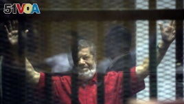 FILE - Former Egyptian President Mohammed Morsi, wearing a red jumpsuit that designates he has been sentenced to death, raises his hands inside a defendants cage in a makeshift courtroom at the national police academy, in an eastern suburb of Cairo.