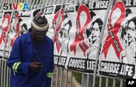 A man makes a call on a mobile phone as he passes past a World AIDS Day banners on the perimeter of an office building in Sandton, Johannesburg, South Africa, Dec. 1, 2014. (AP Photo/Denis Farrell)      