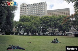 Zimbabweans rest at a park outside Meikles Hotel in central in Harare, February 24, 2015.