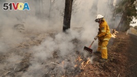 A firefighter uses a rake to move burning debris as he battles a fire near Burrill Lake, Australia, Sunday, Jan. 5, 2020. (AP Photo/Rick Rycroft)