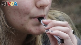 FILE - A high school student uses a vaping device near a school campus in Cambridge, Mass.
