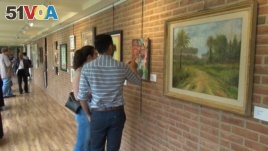 Visitors study some of the works on display in the refugee exhibit at the Sandy Spring Museum in Maryland. Many of the works depict scenes from the artists' home countries.
