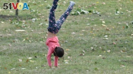A young girl walks on her hands through the grass.