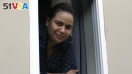 In this Wednesday, May 20, 2020, photo, Wendy De Los Santos, originally from Dominican Republic, stands for a photograph in a window of her home, in Malden, Mass. The 38-year-old Massachusetts resident passed her test to become a U.S. citizen in mid-March. (AP Photo/Steven Senne)