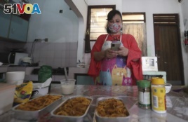 Rani Nurwitawati checks her mobile phone as she prepares food for her online customers at her residence in Bekasi on the outskirts of Jakarta, Indonesia, Nov. 26, 2020.