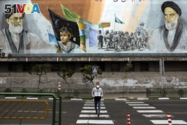 In this Friday, April 3, 2020 photo, a man crosses an empty street under portraits of the late Iranian revolutionary founder Ayatollah Khomeini, right, and Supreme Leader Ayatollah Ali Khamenei, left, in Tehran, Iran.