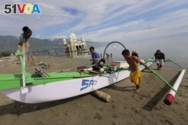 In this April 3, 2019, photo, local fishermen pull a boat to the beach as a mosque heavily damaged by the 2018 earthquake and tsunami is seen in the background in Palu, Central Sulawesi, Indonesia.