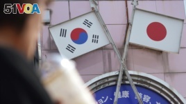 A woman walks past an advertisement with Japanese and South Korean flags at a shop in Shin Okubo area in Tokyo Friday, Aug. 2, 2019. 