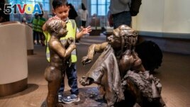 FILE - A boy pats the head of a sculpture of a Neanderthal boy, inside the Smithsonian Hall of Human Origins, Thursday, July 20, 2023, at the Smithsonian Museum of Natural History in Washington.(AP Photo/Jacquelyn Martin)