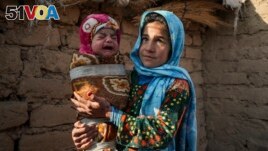 Qandi Gul holds her brother outside their home housing those displaced by war and drought near Herat, Afghanistan. Dec. 16, 2021. Gul's father sold her into marriage without telling his wife, taking a down-payment so he could feed his family. (AP Photo/Mstyslav Chernov)
