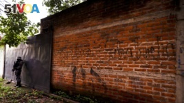FILE - In this Oct. 10, 2019, file photo police guard next to a graffiti wall with the name of a gang as part of a routine patrol in Lourdes, La Libertad, El Salvador. (AP Photo/Eduardo Verdugo, File)
