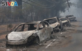 FILE - Burned cars left by their drivers sit along a road in Paradise, California after a wildfire burned much of the town in November of 2018.