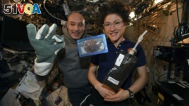 In this photo made available by U.S. astronaut Christina Koch via Twitter on Dec. 26, 2019, she and Italian astronaut Luca Parmitano pose for a photo with a cookie baked on the International Space Station. Researchers want to inspect the handful of...