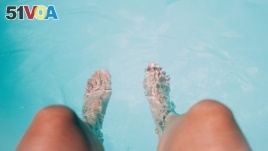 A woman rests at a swimming pool and cools her feet.