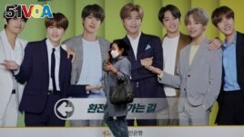 A woman wearing a face mask to help protect against the spread of the coronavirus walks by a board showing members of South Korean K-Pop group BTS to advertise a local bank's money exchange in Seoul, South Korea, Wednesday, Sept. 30, 2020. (AP Photo...