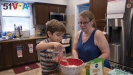 Logan Strauss, 5, adds water to a cake mix while baking with his mother Karen at their home in Basking Ridge, N.J., Wednesday, July 28, 2021. Logan will continue with remote learning from home until he can get the COVID-19 vaccination. (AP Photo/Mark Lennihan)