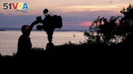 A member of a TV crew adjusts their camera while filming near the shore of Bailey Island, Maine, where a woman swimming off the coast was killed in an apparent shark attack Monday, July 27, 2020. (AP Photo/Jim Gerberich)