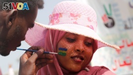 A Sudanese protester waits for a man to finish a painting of the Sudan's old national flag on her face
