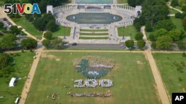 People on the National Mall in Washington, looking toward the World War II Memorial, Aug. 25, 2016, recreate a giant, living version of the National Park Service emblem, using brown, green and white umbrellas. 