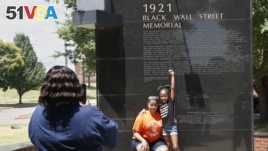 Katrina Cotton, center, of Houston, poses for a photo with her daughter, Kennedy Cotton, age seven, as her aunt, Janet Wilson, left, takes the photo, at the Black Wall Street memorial in Tulsa, Okla., Monday, June 15, 2020. (AP Photo/Sue Ogrocki)