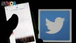 A man reads tweets on his phone in front of a displayed Twitter logo in Bordeaux, southwestern France, March 10, 2016.