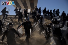 Mexican police run as they try to keep migrants from getting past the Chaparral border crossing in Tijuana, Mexico, Sunday, Nov. 25, 2018, near San Ysidro, California.