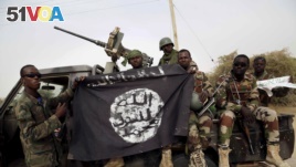 FILE PHOTO - Nigerian soldiers hold up a Boko Haram flag that they had seized in the recently retaken town of Damasak, Nigeria.