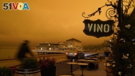 FILE - In this Sept. 9, 2020, file photo, a bicyclist rides past a seating area outside a wine bar as smoke from wildfires darken the morning sky in Sausalito, California.