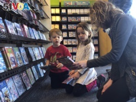 Elizabeth Gilless, of Memphis, Tenn., shows her children John, 3, and Ellen, 5, a movie from the children's section at the last Blockbuster on the planet in Bend, Ore., on Tuesday, March 12, 2019. (AP Photo/Gillian Flaccus)