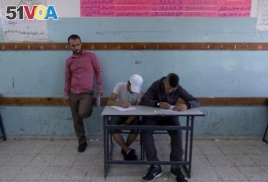 In this Sunday, May 26, 2019 photo, a teacher supervises while two Palestinian school children attend a final exam at the United Nations Relief and Works Agency for Palestine Refugees in the Near East, UNRWA, Hebron Boys School.